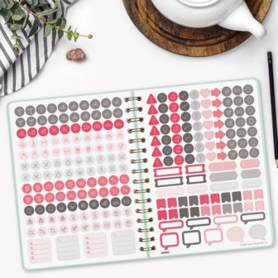 Caderno aberto com autocolantes organizadores multicoloridos numa mesa com utensílios de escrita e decoração