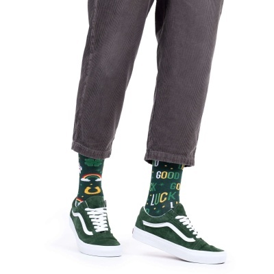 Meias verdes estampadas com trevo, arco-íris, ferradura e texto, calças cinza e ténis verdes com detalhe branco.