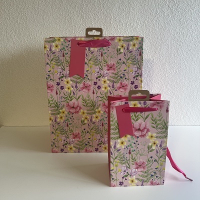 Dupla de sacolas de papel com padrão floral em fundo rosa e alças de fita rosa