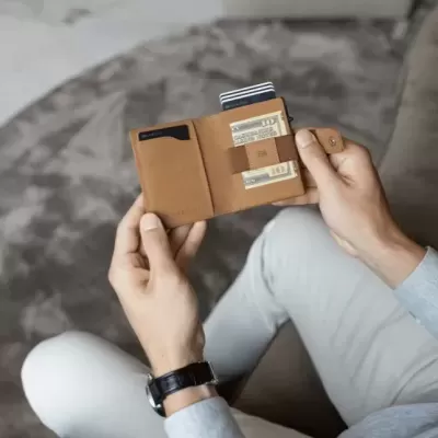 Carteira de pele castanha aberta com cartões, mãos segurando, ambiente interior com carpete e sofá