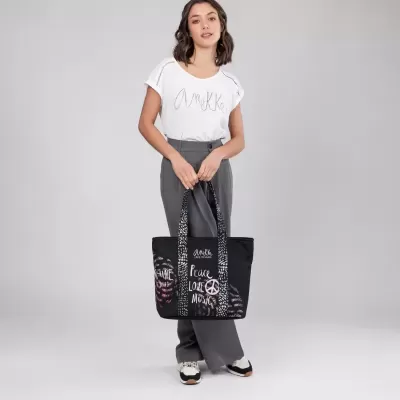 Mulher com t-shirt branca e calças cinzentas a segurar mala preta com inscrições.