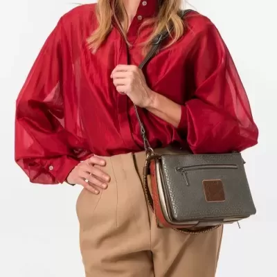 Mulher com sacola castanha escura e bege, blusa vermelha transparente e calças castanho claro