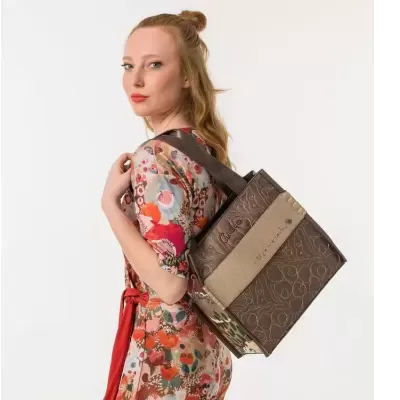 Mala castanha com padrão floral e faixa bege usada por mulher de vestido colorido