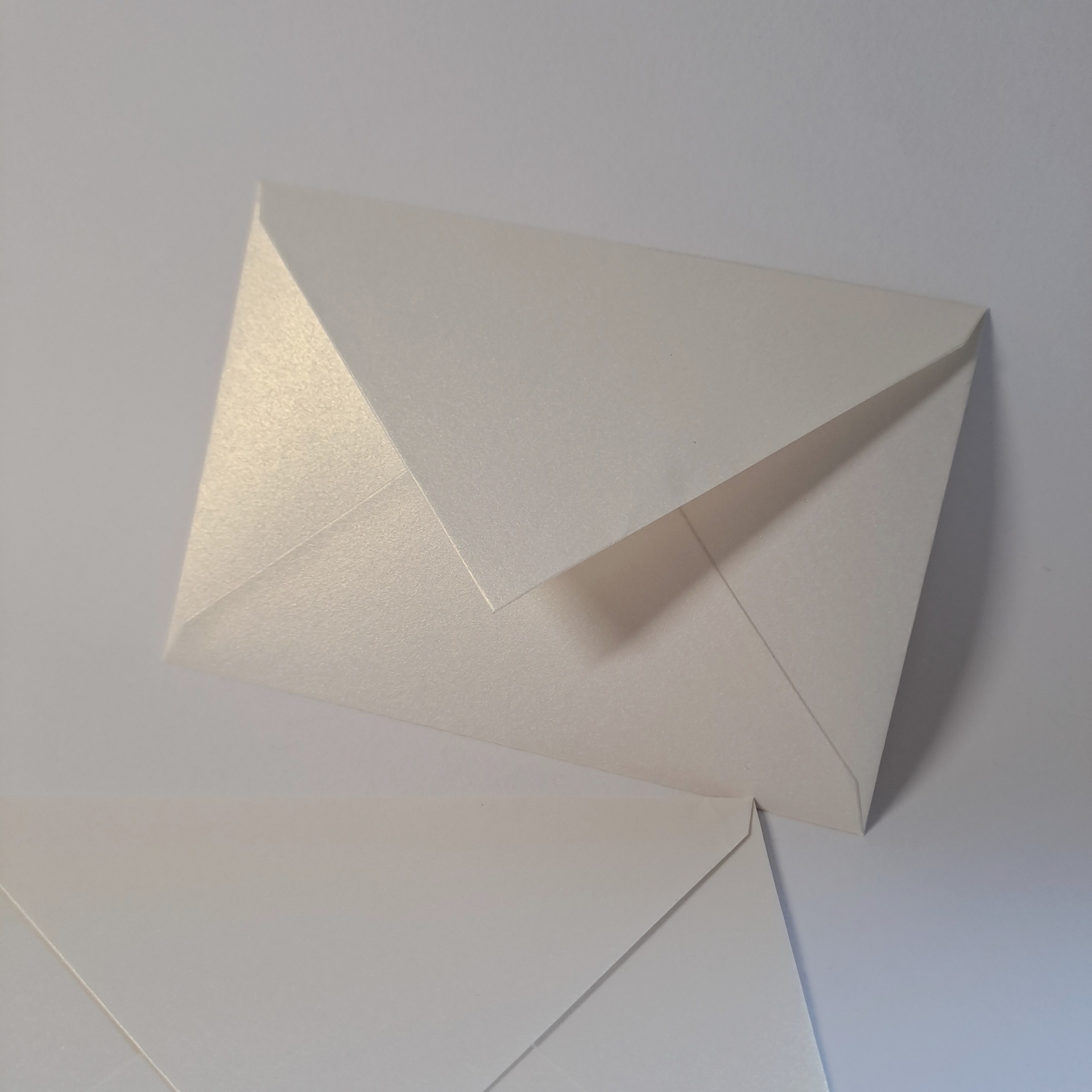 Pacote 50 Envelopes Montesinho metallic C6 Dois envelopes brancos com textura lisa e brilho sobre superfície branca.