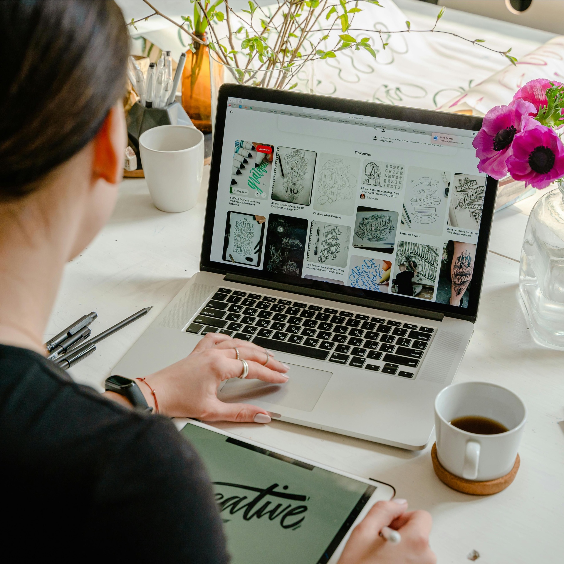 Pessoa a usar computador portátil e tablet digitalizador numa mesa com canecas, canetas e flores