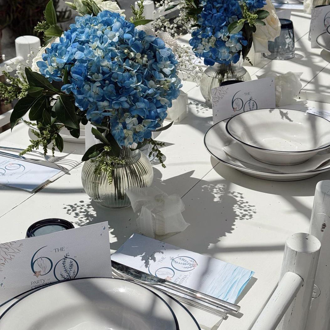 Arranjos florais azuis e mesa posta branca com loiça e talheres
