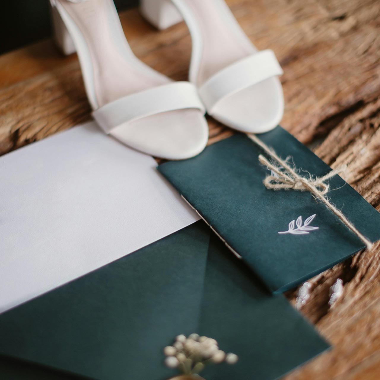 Sandálias brancas de salto grosso e envelopes em papel escuro e claro sobre madeira rústica