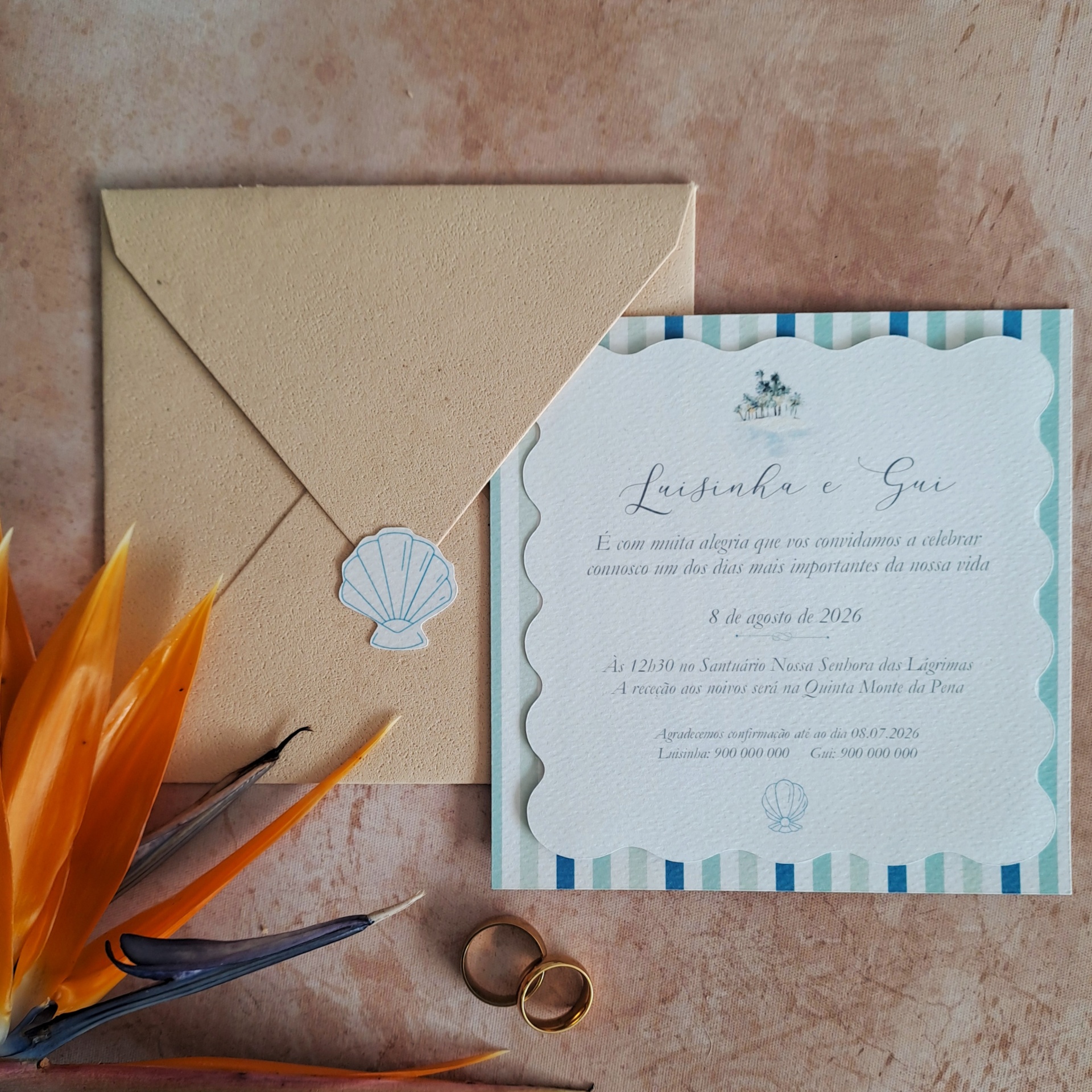 Convite de casamento em papel branco texturizado com bordas onduladas e riscas azuis junto a envelope castanho com selo de concha.