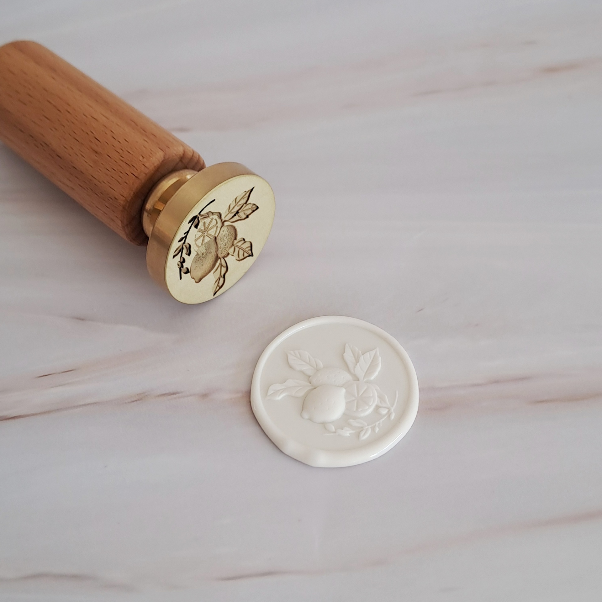 Carimbo de lacre metálico com desenho de limões e impressão de cera branca com o mesmo desenho