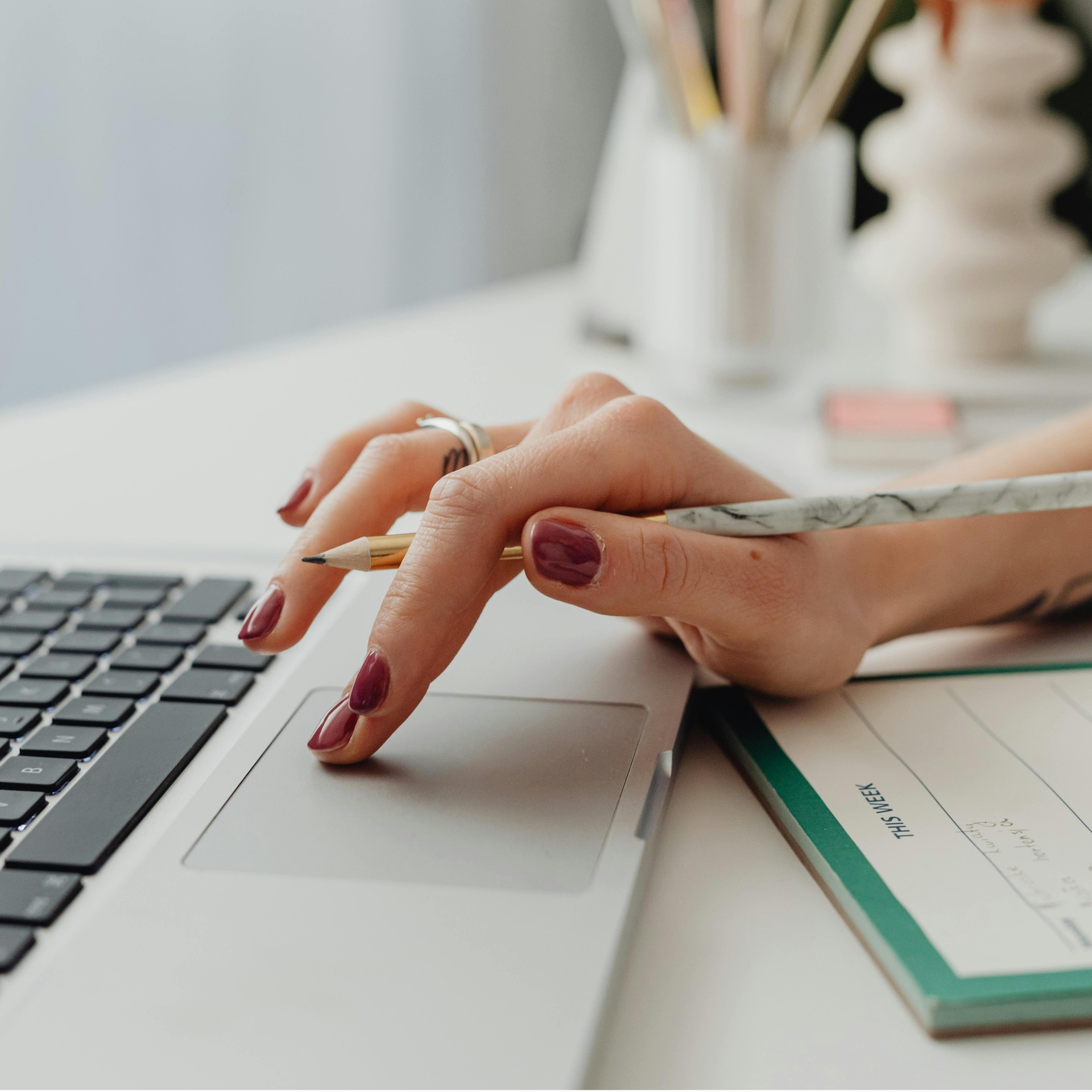 Mão feminina com esmalte vinho a usar touchpad de portátil prateado com lápis e calendário semanal