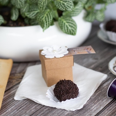 Caixa pequena de papel castanho com flor branca e brigadeiro com granulado de chocolate