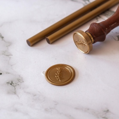 Selo de cera dourado com carimbo e varetas de cera em superfície de mármore