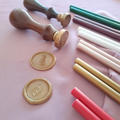 Carimbos de lacre em madeira com bastões coloridos para lacre e dois selos estampados sobre superfície rosa