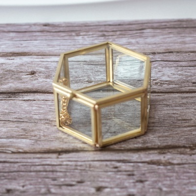 caixa hexagonal de vidro com estrutura dourada sobre madeira clara