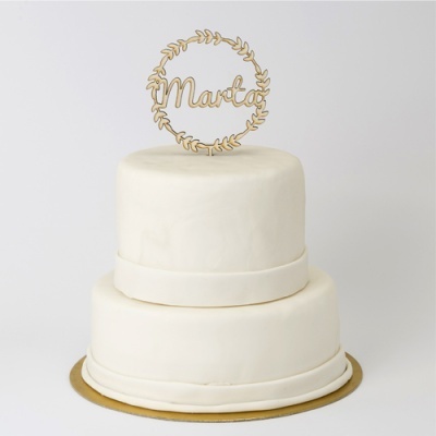 Bolo branco de dois andares com topo decorativo em madeira dourada com a palavra 'Maria'.