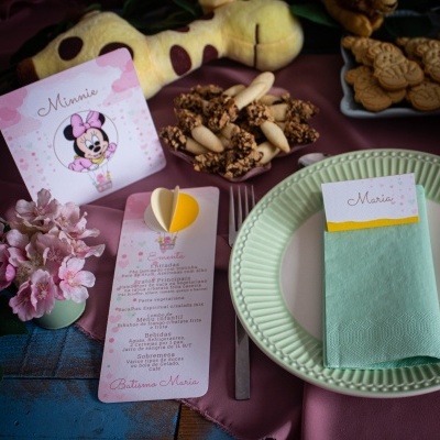 Mesa decorada para batizado com prato verde, guardanapo, cartões Minnie e Maria, flores e peluche girafa