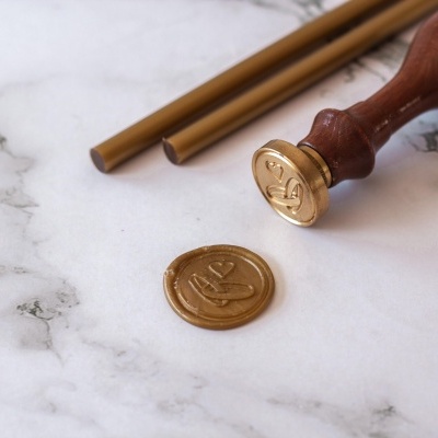 Carimbo de selo de cera com selo dourado e varetas de cera em superfície branca