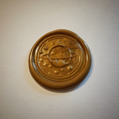 Selo de cera dourada com desenho circular e esfera central