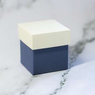 Caixa quadrada pequena creme e azul sobre superfície branca com padrão marmoreado