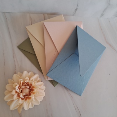 Cinco envelopes coloridos e flor artificial sobre superfície de mármore