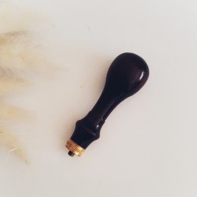 Cabo de madeira escura com peça metálica dourada numa superfície branca.