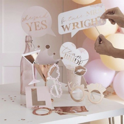 Adereços de festa em papel e madeira com textos e símbolos relacionados a casamento em mesa branca com balões atrás