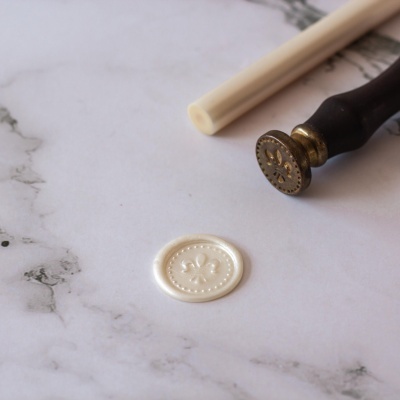 Selo de lacre branco com carimbo de metal e pavio sobre superfície marmoreada.