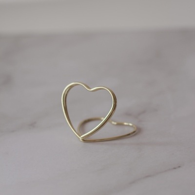 Anel aberto em forma de coração dourado sobre superfície marmorizada