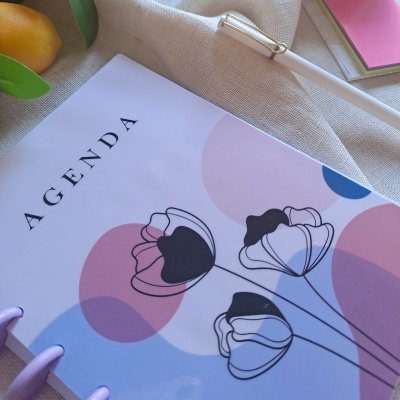 Agenda com capa floral colorida e caneta branca sobre tecido bege