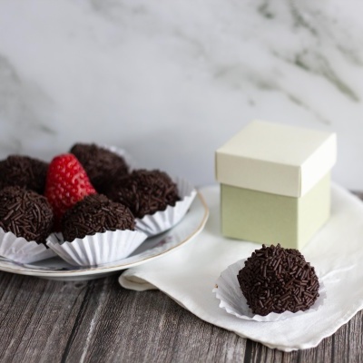 Brigadeiros com granulado de chocolate em prato branco e caixa pequena branca