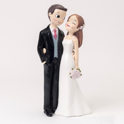 Figura decorativa de noivos em casamento, ele veste fato preto, camisa branca, gravata vermelha e colete azul claro, ela usa vestido branco longo e segura um bouquet de flores cor-de-rosa