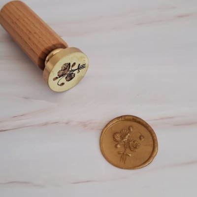 Selo de cera com cabo de madeira e impressão dourada numa superfície clara