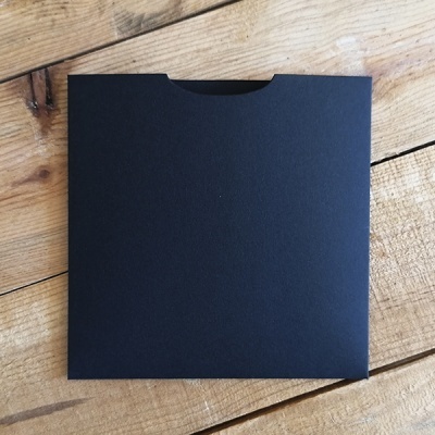 Envelope preto quadrado de cartão fosco com recorte semicircular numa superfície de madeira clara