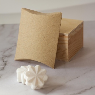 Sabonetes brancos em forma de flor ao lado de caixas de cartão castanho e madeira clara sobre superfície mármore.