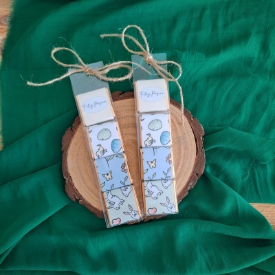 Dois marcadores de livros com ilustrações coloridas e laços de corda sobre madeira e tecido verde