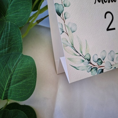 Calendário branco com decoração de folhas verdes, colocado ao lado de folhas artificiais verdes