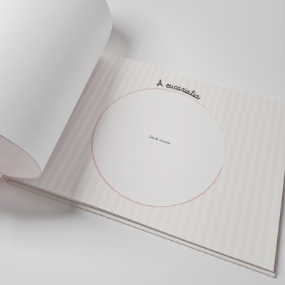 Página de livro infantil aberta com espaço circular para foto da comunhão e texto 'A eucaristia'