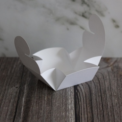 Caixa branca de papel para embalagem aberta com abas arredondadas sobre mesa de madeira