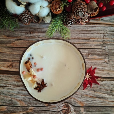 Vela redonda branca com especiarias em recipiente metálico sobre mesa de madeira com decoração natural