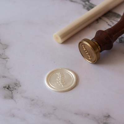 Selo de cera branco com padrão de folha junto a carimbo de madeira e metal sobre mármore branco