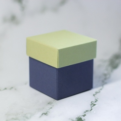 Caixa quadrada de papel azul e amarela clara sobre superfície branca com veios cinzentos