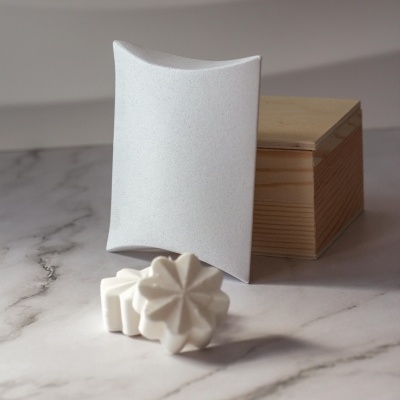 Caixa almofada branca com sabonetes brancos florais e caixa de madeira clara sobre mármore