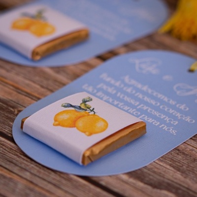 Pequenos chocolates embrulhados em folha dourada com rótulos de limões em papel branco, sobre etiquetas azuis.