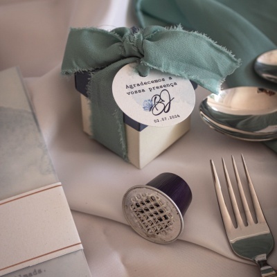 Caixa pequena com fita verde e etiqueta personalizada numa mesa com talheres e cápsula de café
