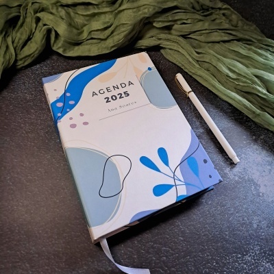 Agenda 2025 com capa abstrata azul e caneta branca sobre superfície escura