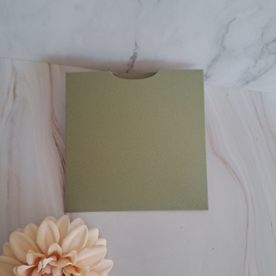 Envelope verde texturizado sobre superfície de mármore com flor artificial creme ao lado.