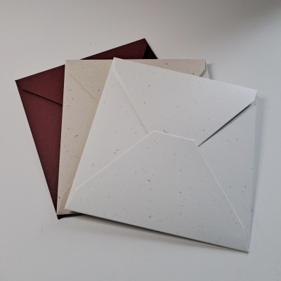 Três envelopes de papel reciclado em branco, bege e castanho sobre superfície branca