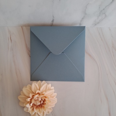Envelope cinzento texturizado com flor cor de pêssego numa superfície branca com veios