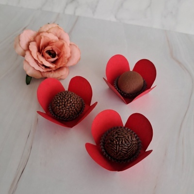 Três brigadeiros em forminhas vermelhas e uma flor rosa artificial