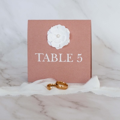 Cartão de mesa rosa com flor branca e anéis dourados